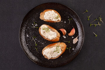 Flat lay composition with bread and garlic spread on black plate.