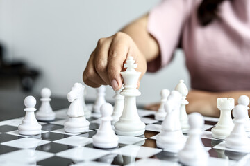 Businesswoman holding white chess pieces on a chessboard, comparing chessboard to business administration, planning operations to achieve goals and problem-solving. Business administration concept.