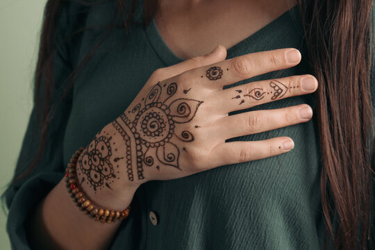 Woman with beautiful henna tattoo on hand against green background, closeup. Traditional mehndi