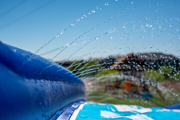 Selective focus on water spray shooting across a slip and slide perched on the top of a hill