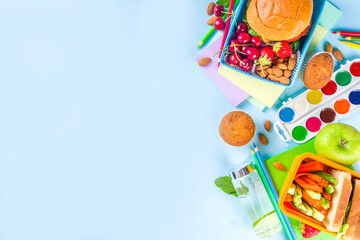 Back to school, Healthy tasty kid lunch box with sandwiches, nuts, fresh fruits and vegetable sticks. With school supplies, pencils, notebooks, on bright blue background flatlay top view copy space