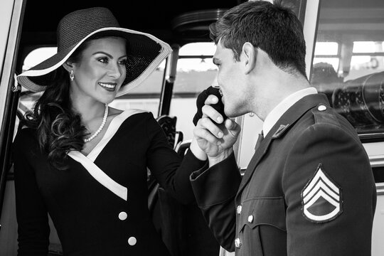 Vintage beautiful woman wearing hat is helped off retro bus by soldier in wwii uniform