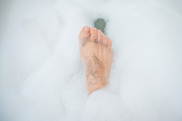 Funny picture of a man taking a relaxing bath. Close-up of male feet in a bubble bath