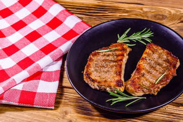 Plate with roasted steaks and rosemary twigs on a wooden table
