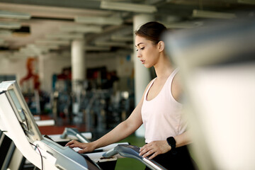 Athletic woman adjusting speed on treadmill while working out in a gym.