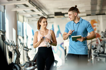 Happy fitness instructor and athletic woman communicating while walking through gym.