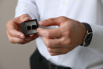 Stylish man holding box with cufflinks against beige background, closeup