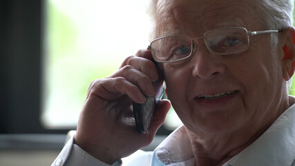 Elderly man sit in chair and speak on phone in modern apartment