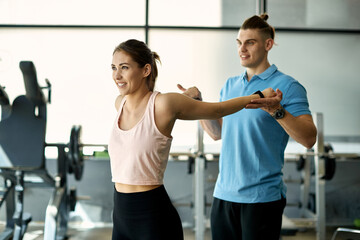 Fototapeta na wymiar Smiling athletic woman doing stretching exercise with assistance of her personal trainer in a gym.