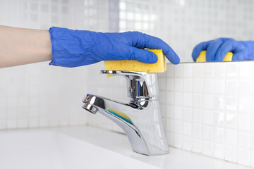 Woman doing chores in bathroom, cleaning of water tap with sponge