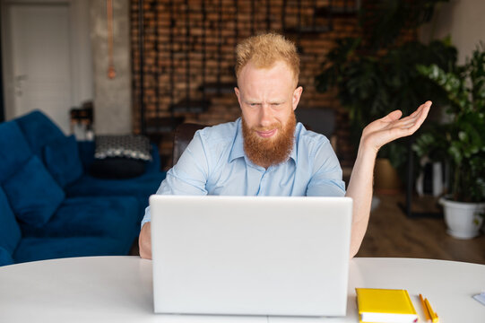Puzzled and confused redhead bearded male entrepreneur staring at the laptop screen, a bearded man in smart casual shirt looking at monitor with asking expression, misunderstanding what happened