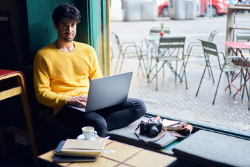 Pensive ethnic man working on laptop
