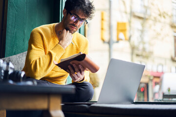 Pensive ethnic man writing thoughts in notepad