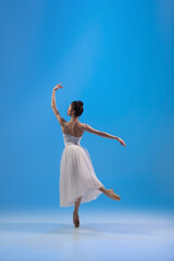 Fototapeta premium Young and incredibly beautiful ballerina is posing and dancing at blue studio full of light.