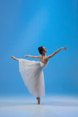 Young and incredibly beautiful ballerina is posing and dancing at blue studio full of light.