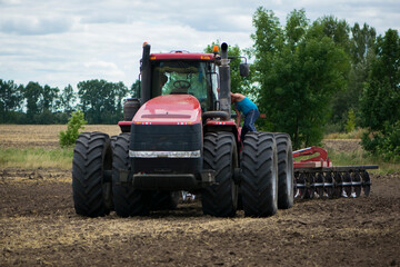Obraz premium tractor driver near a large red tractor. A farmer on a tractor prepares land for a seeding tractor with a plow in an agricultural field. August, Ukraine