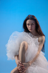 Tired ballet dancer sitting over blue studio background