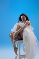 Fototapeta na wymiar Tired ballet dancer sitting over blue studio background
