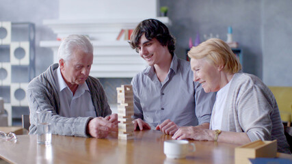 Young man with grandparents having fun building tower from wooden blocks