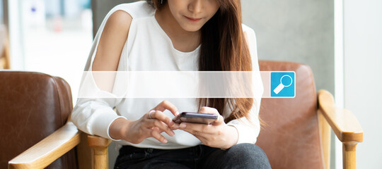 Asian woman sitting in coffee shop and using a smartphone for searching information on the...