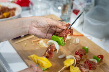 BBQ meal preparation in kitchen, action of people hand's is skewer a pork or beef meat into the metal stick. Food preparation photo, close-up and selective focus.