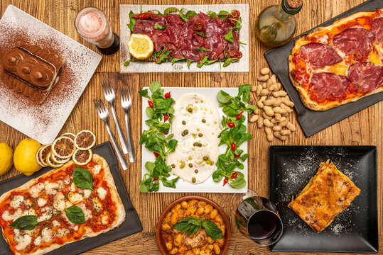 Top view image of Italian food plates with forks, pizzas, carpaccio  and wine