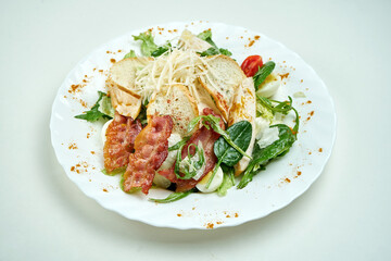 Classic caesar salad with lettuce, spinach, chicken, croutons, parmesan and bacon in a white plate on a white plate