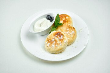 Ukrainian sweet dish - cottage cheese pancakes with sour cream on a white plate on a white background. Sweet syrniki