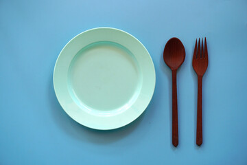 Empty plate with spoon and fork on blue background.