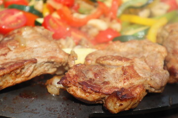 Grilling in a cast iron pan. Meat - pork neck with vegetables: onion, mushrooms, colorful peppers and zucchini
