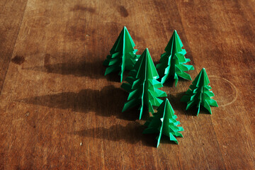 Christmas trees origami on rustic wood background with long shadows.
