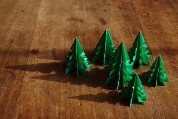 Christmas trees origami on rustic wood background with long shadows.
