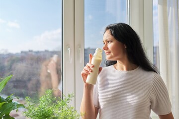 Woman drinking milk drink from bottle standing near window, milk yogurt dairy healthy drinks
