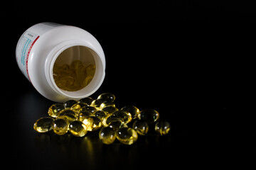 Bottle with pills, capsules, of cod liver oil spilling out, isolated on black background