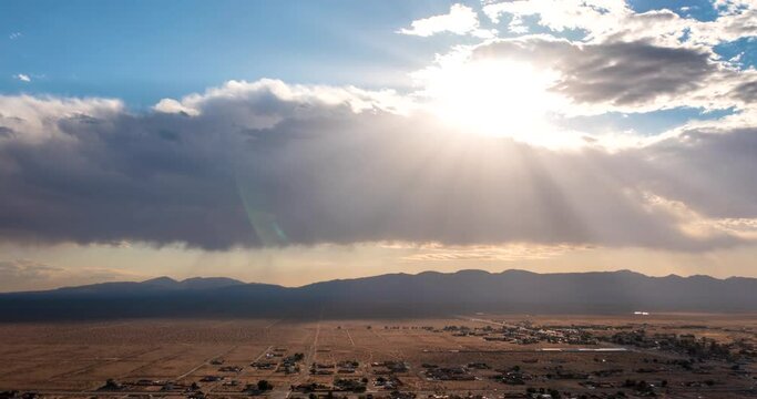 Aerial time lapse over California City with the sun shinning through the clouds and rays of sun casting light and shadow over the community in the valley