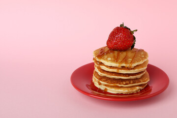 Plate with pancakes with strawberry and caramel on pink background