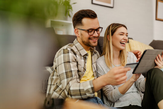 Smiling couple shopping online, man holding a credit card while woman doing a payment.