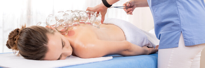 Cupping Therapy Banner. Young female physiotherapist applying glass suction banks on back of her patient, during cupping therapy, closeup detail.