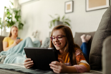 Little cute smiling girl reading e-book and lying on the sofa.