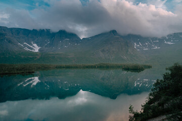 Fototapeta na wymiar Foggy mountains are reflected in the mirror surface of the lake in polar summer. Mountain landscape in Kola Peninsula, Arctic