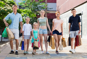 Positive cheerful man and woman with four kids walking and holding shopping bags in town