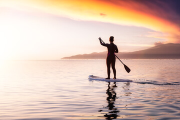 Adventurous girl on a paddle board is paddeling in the Pacific West Coast Ocean. Sunset Sky Art Render. Taken near Spanish Banks, Vancouver, British Columbia, Canada.