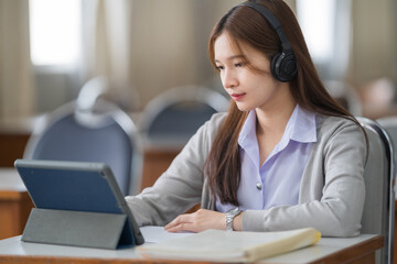 Young interactive happy Asian teenage girl university student studying and presenting her lesson online via video call on a digital tablet in the classroom alone herself. Education stock photo