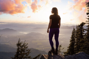 Adventurous Caucasian Adult Woman hiking in Canadian Nature over looking mountainous landscape. Sunset Sky Art Render. Elk Mountain Hike in Chilliwack, East of Vancouver, BC, Canada.