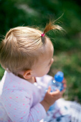 Little girl with a ponytail holds a plastic bottle in her hands. Top view