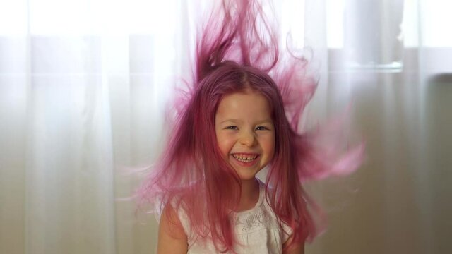 Fun crazy girl smile looks at camera. Happy child with flying pink hair. Little daughter laughs at home. Happy and healthy childhood. Close up of pretty attractive optimistic lovely have free freedom