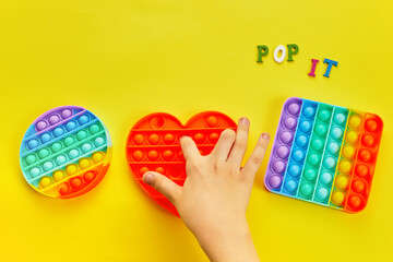 Kid hands playing with colorful pop It fidget toy. Colorful antistress sensory toy fidget push pop it. - obrazy, fototapety, plakaty