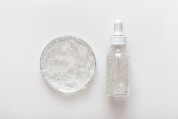 Close-up transparent cosmetic gel in glass petri dish with bottle pipette on white background....