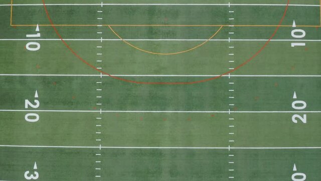 Football or soccer field. Top down aerial reveals yard markers and numbers. Rising shot of empty playing grass turf field.