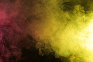 Artificial magic smoke in red-yellow light on black background
